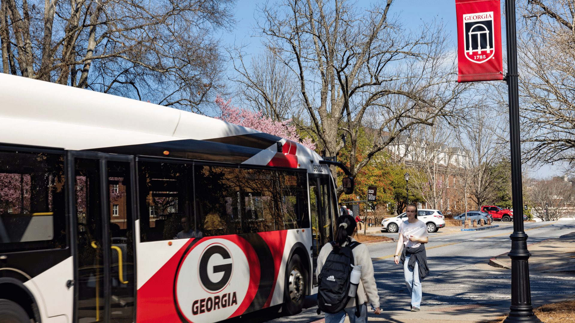 A campus bus passes under a Arch shield logo light pole banner on Sanford Drive.